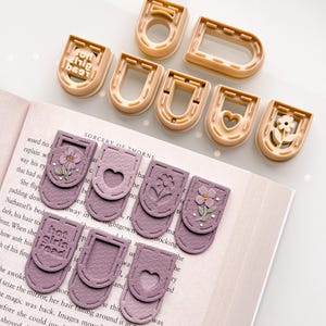 May include: A collection of beige U-shaped molds and lavender-colored book page holders. The page holders feature floral and heart designs, with the text "hot girls read" on one. Ideal for book lovers.
