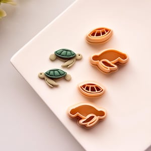 May include: Two plastic turtle cookie cutters, one green and one brown, and two plastic turtle shell cookie cutters, both brown.