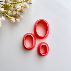 May include: Three pink plastic oval-shaped cookie cutters of different sizes.