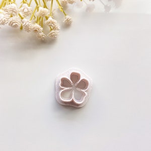 May include: White plastic flower cookie cutter with a five-petal flower design.