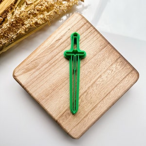 Pode incluir: Cortador de biscoitos de espada de plástico verde em uma superfície de madeira.