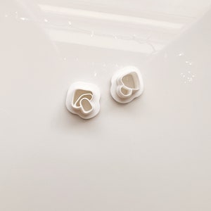 May include: Two white plastic cookie cutters, one shaped like a heart and the other shaped like a flower.