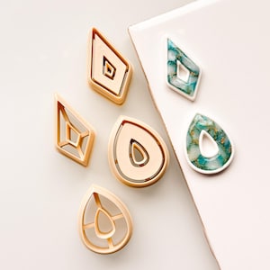 May include: Five cookie cutters in the shape of a teardrop with an inner teardrop shape, and a diamond shape with an inner diamond shape. Two teal resin earrings in the shape of a teardrop and a diamond.