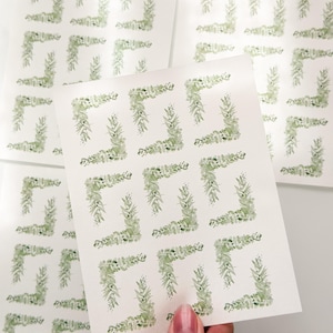 May include: A set of white sticker sheets featuring a repeating pattern of watercolor-style green eucalyptus leaf corner frames. Each sheet contains multiple rectangular arrangements of botanical foliage in various shades of sage and forest green.