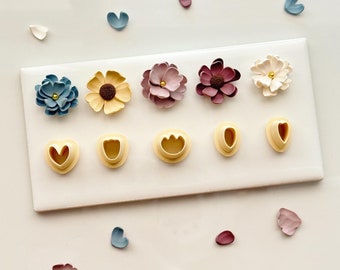 May include: A set of six flower-shaped cookie cutters, including a heart, a daisy, and a flower with five petals. The cutters are arranged on a white surface with several loose flower-shaped cookie cutters in various colors.
