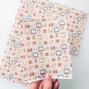 May include: A rectangular sheet of paper featuring a repeating grid pattern of small squares. Each square contains illustrations of open books, stacks of books, pink roses, and blue teacups set against soft pink, blue, and white checkered backgrounds.