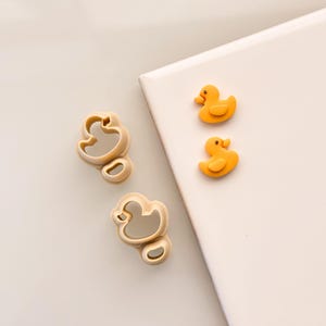 May include: Three yellow rubber duck cookie cutters and two plastic duck cookie cutters on a white surface.