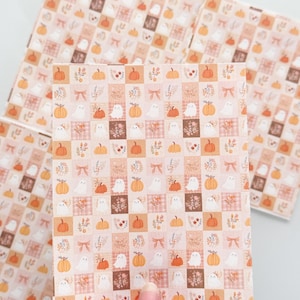 May include: A rectangular sheet of paper featuring a repeating grid pattern of small squares. The design includes illustrations of orange pumpkins, white ghosts, brown bows, and autumn foliage in shades of tan, brown, and soft orange.