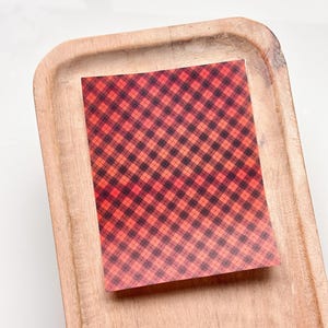 Peut inclure: Une feuille de papier à motif écossais rouge et noir. Le papier présente un effet dégradé, la couleur rouge passant à une nuance d'orange plus claire en haut.