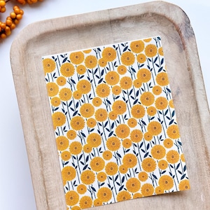 May include: A white card with a repeating pattern of yellow flowers with dark green stems and leaves.