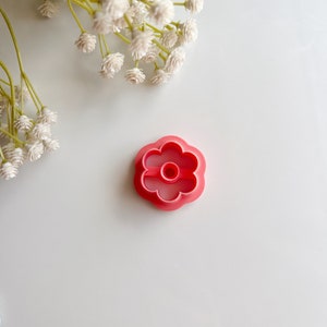 May include: A pink plastic flower-shaped cookie cutter with a center hole.