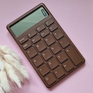 Puede incluir: Una calculadora marrón con una pantalla digital y un teclado numérico. La calculadora tiene las siguientes teclas: ON/AC, MRC, M-, M+, GT, √, +, 7, 8, 9, X, 4, 5, 6, -, 1, 2, 3, +, 0, =.