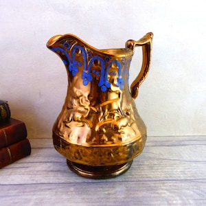 May include: A copper jug with a blue and gold floral design. The jug has a textured surface and a wide base.