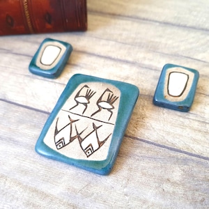 Pode incluir: Um conjunto de três brincos de cerâmica com esmalte azul e desenhos brancos. Os brincos apresentam um design de peixe estilizado e uma forma oval simples.