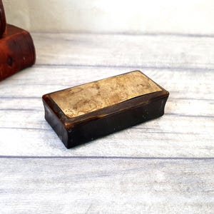 May include: A small, rectangular box made of dark brown wood with a light brown top. The top has a worn, aged look.