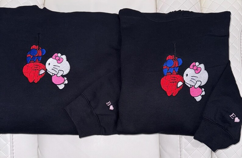 Pu&ograve; includere: Due felpe nere con disegni ricamati. Uno presenta un Spider-Man rosso e blu e una Hello Kitty bianca con un vestito rosa. L'altro ha lo stesso design. Entrambe le maniche hanno una lettera e un cuore.