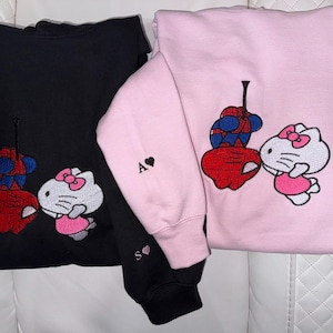 Pu&ograve; includere: Due felpe con cappuccio, una nera e una rosa, con disegni ricamati. I disegni raffigurano un supereroe rosso e blu che bacia un personaggio di Hello Kitty. La felpa rosa ha la lettera "A" e un cuore sulla manica, e la felpa nera ha le lettere "S" e un cuore.