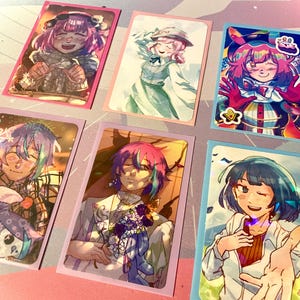 May include: Six colorful anime-style character art cards. Each card features a different character with vibrant hair and clothing. The cards have a holographic effect and are set against a light background. The characters are smiling and winking.