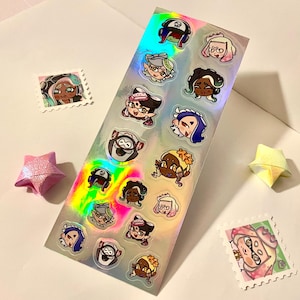 Puede incluir: Una hoja de pegatinas holográficas iridiscentes con varios personajes de dibujos animados con diferentes expresiones. Los personajes llevan todos sombreros y tienen ojos grandes. Las pegatinas están dispuestas en una cuadrícula sobre un fondo blanco.