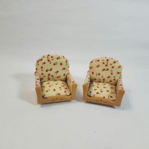 May include: Two miniature armchairs. The chairs feature a light beige fabric patterned with red cherries and green leaves. The frames are light brown. The chairs are set against a white background.