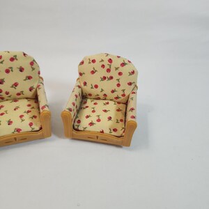May include: Two miniature armchairs. The chairs feature a light yellow fabric with a red cherry pattern. The armrests and frame are light brown. These chairs are designed for a doll's house or similar miniature setting.