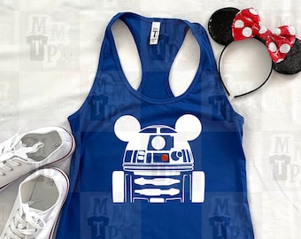 Könnte beinhalten: Ein blaues Tanktop mit einer weißen Silhouette von R2-D2 mit Mickey-Maus-Ohren. Das Tanktop liegt auf einer weißen Oberfläche.