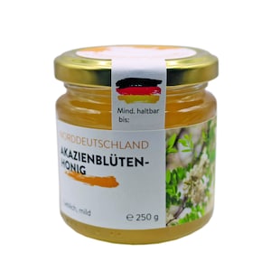 May include: A glass jar of honey with a white label that reads "Norddeutschland Akazienblüten-Honig" and "e 250 g". The label also has a German flag and the text "Mind. haltbar bis:".