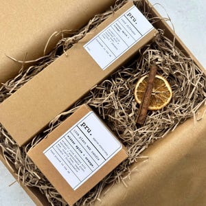 Op de afbeelding: Een cadeaudoos gevuld met bruin versnipperd papier, een bruine kaars met de tekst "pru. 100% plant wax candle winter spice orange. approx. 140g/180g" en een bruine rietdiffuser met de tekst "pru. reed diffuser winter spice orange. aromatic oils blended with a vegan base. alcohol + paraben free. handmade in the uk. 100ml".