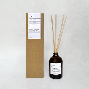 Könnte beinhalten: Ein brauner Karton mit einem weißen Etikett, auf dem "pru. Entspannung. Schilfdiffusor Ylang Ylang, Orange Geranie + Lavendel 100% ätherische Öle Aromatische Öle, die mit einer veganen Basis, alkoholfrei und parabenfrei gemischt werden, handgefertigt in Großbritannien 100 ml" steht, und eine braune Glasflasche mit einem weißen Etikett, auf dem "pru. Entspannung. Ylang Ylang, Orange Geranie + Lavendel 100% ätherische Öle" steht, sowie braune Holzstäbchen in der Flasche.