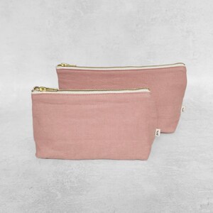 May include: Two pink linen zippered pouches with white lining. The pouches are nested together, with the larger pouch on top. The pouches have a gold zipper and a small label with the text "P.T.U."