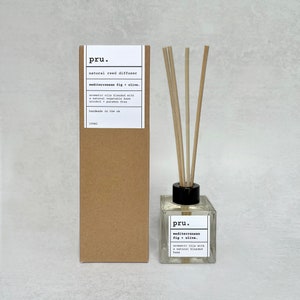 May include: A brown cardboard box with a white label that reads "pru. natural reed diffuser mediterranean fig olive. aromatic oils blended with a natural vegetable base alcohol paraben free handmade in the uk 100ml" and a clear glass bottle with a black lid and a white label that reads "pru. mediterranean fig olive. aromatic oils with a natural blended base".