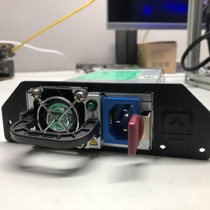 May include: A black computer power supply unit with a green fan, a blue power cord, and a red key switch. The unit has a handle and is mounted on a black bracket.
