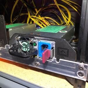May include: A black power supply unit with a green label and a blue and pink connector. The power supply is mounted in a server rack with yellow cables.