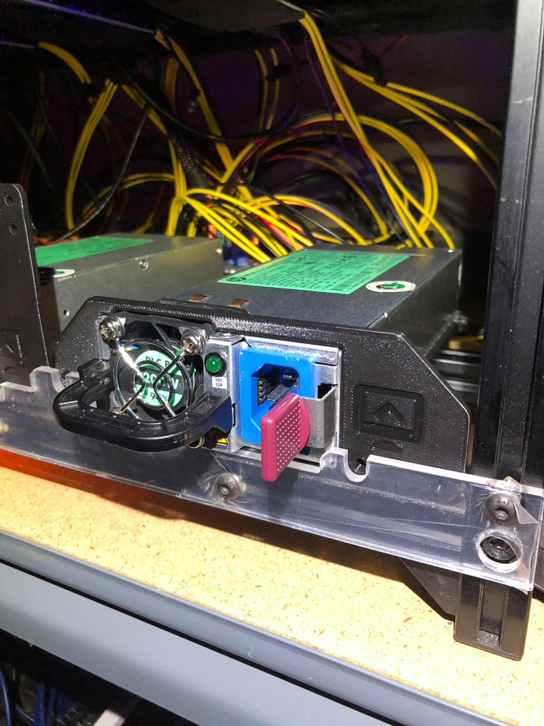 May include: A black power supply unit with a green label and a blue and pink connector. The power supply is mounted in a server rack with yellow cables.