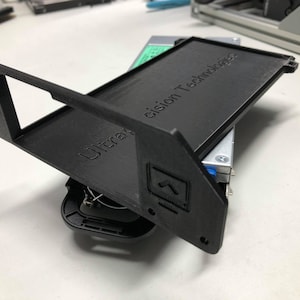 May include: A black 3D printed hard drive enclosure with the text "Ultra Precision Technology" on the top. The enclosure is open and shows a hard drive inside.