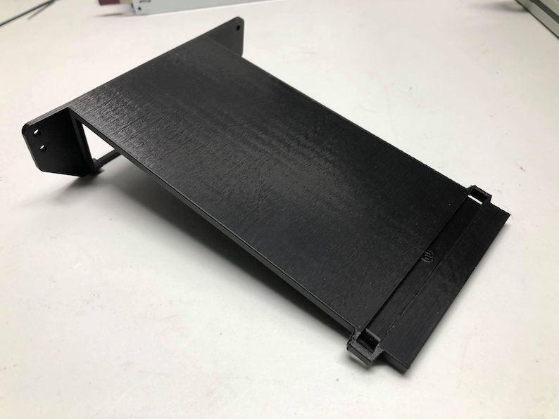 May include: A black 3D printed phone stand with a slot for charging cables. The stand is angled to hold a phone upright.