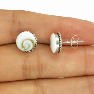 May include: A pair of round stud earrings. Each earring features a white, spiral-patterned center with a silver-colored, twisted rope border. The earring posts are silver-colored.