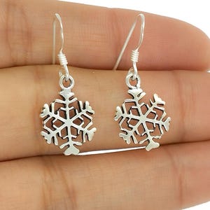 Op de afbeelding: Een paar zilveren sneeuwvlok oorbellen. Elke oorbel heeft een gedetailleerd sneeuwvlokontwerp dat aan een eenvoudige haak hangt. De oorbellen worden tegen een neutrale achtergrond getoond.