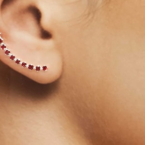 Może przedstawiać: Zbliżenie na ucho z srebrnym kolczykiem w kształcie mankietu ozdobionym rzędem czerwonych kamieni szlachetnych.