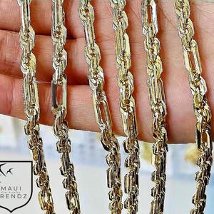 May include: A collection of six gold-toned rope chains featuring a twisted, textured link design with a polished finish. The chains are displayed vertically, showcasing their intricate, interlocking metal segments and reflective surfaces. Includes a logo.