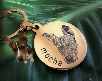 May include: A round gold-toned metal keychain featuring an engraved portrait of a dog and the name mocha. A small brown and white puppy is positioned next to the keychain, and the text Mocha & Si is printed in the lower right corner.