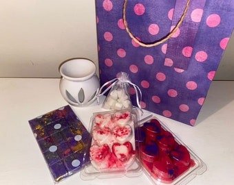 May include: A white ceramic wax warmer, a purple gift bag with pink polka dots, a small organza bag of white wax melts, and three plastic trays containing heart-shaped and rectangular wax melts in shades of purple, red, and white.
