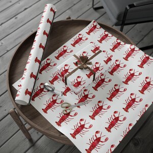 May include: White wrapping paper with a repeating pattern of red lobsters. A brown ribbon is tied around a gift box wrapped in the same paper.