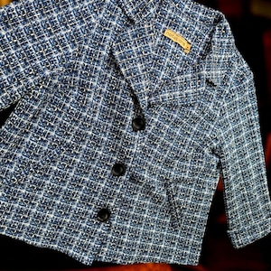 May include: A blue and white tweed blazer with three black buttons and a notched collar. The blazer has three-quarter sleeves and a small tag that reads "notations". The fabric has a woven texture.