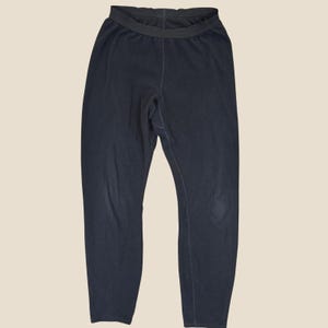 May include: A pair of solid black leggings featuring a high-rise elastic waistband and a fitted silhouette. The fabric has a smooth, matte texture throughout, with visible vertical seam detailing running down the center front and along the inner legs.