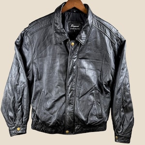 Peut inclure: Une veste en cuir noir dotée d'un col classique, de manches longues avec poignets boutonnés et d'une fermeture à boutons sur le devant. L'étiquette intérieure indique Beyond Sports Classics. La veste possède deux poches latérales et un ourlet élastique.