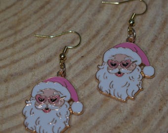 May include: Gold-tone Santa Claus earrings with pink hats and heart-shaped sunglasses. The earrings feature white beards and rosy cheeks. The festive jewelry is designed with gold-coloured ear hooks.