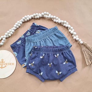 May include: Three pairs of blue and white patterned baby bloomers. The bloomers are made of a soft, comfortable fabric and feature a variety of floral and bee designs.