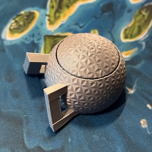 May include: A gray, 3D printed, geodesic dome-shaped object with two handles. The object has a textured surface.