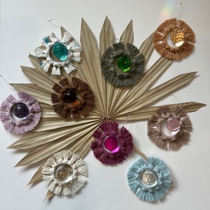 May include: Nine macrame wall hangings with crystal prisms in the center. The hangings are in various colors, including white, brown, pink, blue, and green. Each hanging has a fringe around the edge.